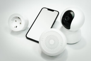 Dispozitive inteligente pentru securitate: camera, telefon si difuzor, alaturi de un detector de fum wireless, pe fundal alb.