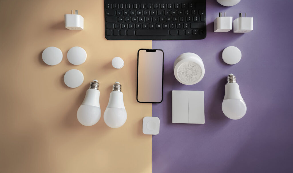 Tastatura, smartphone si camera supraveghere fara fir pe un fundal violet si galben, alaturi de dispozitive electronice moderne.