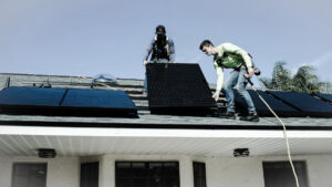 Doi barbati pe un acoperis, lucrand la instalarea panourilor solare pentru a folosi energia solara.